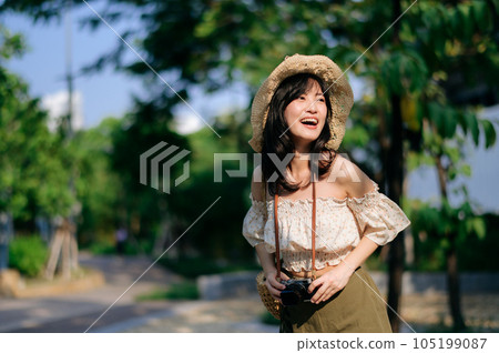 Portrait of asian young woman traveler with weaving hat and basket and a camera on green public park nature background. Journey trip lifestyle, world travel explorer or Asia summer tourism concept. Portrait of asian young woman traveler with weaving hat and basket and a camera on green public park nature background. Journey trip lifestyle, world travel explorer or Asia summer tourism concept. 105199087