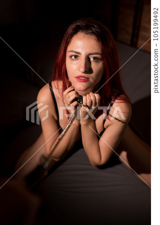 Leather belt on the neck of BDSM. Luxurious chest in black underwear. A woman kneels in sexual games as a victim. Toys for adults. Leather belt on the neck of BDSM. Luxurious chest in black underwear. A woman kneels in sexual games as a victim. Toys for adults. 105199492