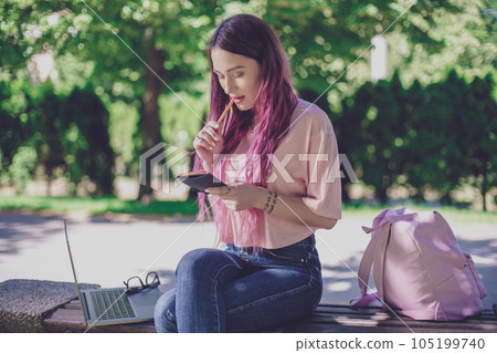 Woman writing in a notebook sitting on a wooden bench in the par 105199740