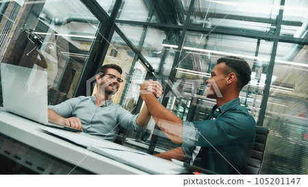 Glad to work with you Two young and handsome men shaking hands and smiling while working in modern office Glad to work with you Two young and handsome men shaking hands and smiling while working in modern office 105201147