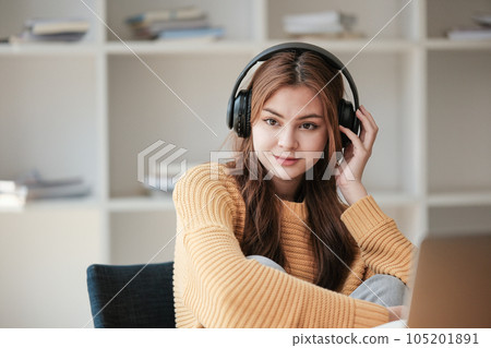 A beautiful caucasian female student is studying in college remotely. She is sitting at a table at home with a laptop and a notepad and concentrated is watching a video conference lesson 105201891