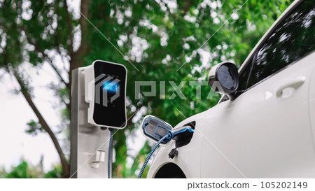 Electric car plugged in with charging station in eco green park. Peruse 105202149