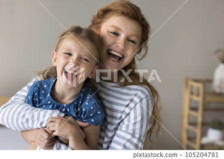 Cheerful red haired mom cuddling, tickling cute kid on sofa 105204781