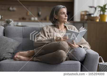 Thoughtful calm grey haired reader woman resting on comfortable sofa Thoughtful calm grey haired reader woman resting on comfortable sofa 105204800