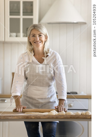 Happy pretty blonde mature baker woman in apron rolling dough Happy pretty blonde mature baker woman in apron rolling dough 105204939