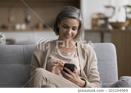 Cheerful beautiful mature woman using application on smartphone Cheerful beautiful mature woman using application on smartphone 105204969