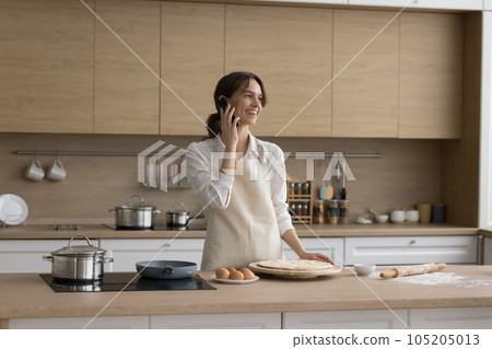 Woman talking on cellphone while cook homemade pizza in kitchen Woman talking on cellphone while cook homemade pizza in kitchen 105205013
