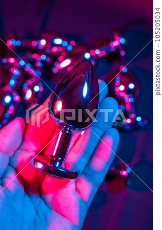 Man holding metal anal plug in neon pink purple light. Man holding metal anal plug in neon pink purple light. 105205034