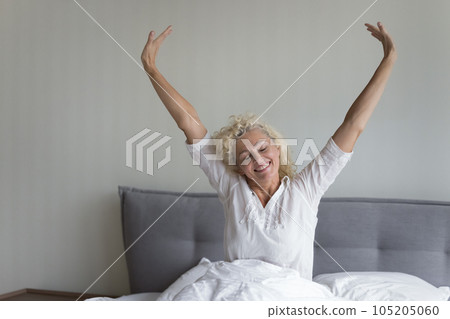Cheerful blonde mature woman awaking in fresh white linen Cheerful blonde mature woman awaking in fresh white linen 105205060
