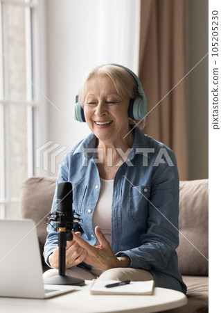 Vertical portrait happy 65s woman in headphones speaks into microphone Vertical portrait happy 65s woman in headphones speaks into microphone 105205230