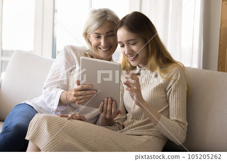 Cheerful teen grandchild girl and happy grandmother holding tablet Cheerful teen grandchild girl and happy grandmother holding tablet 105205262
