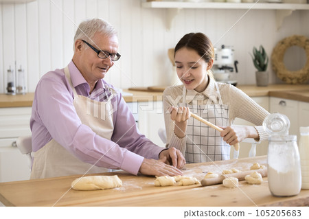 Positive teenage girl in apron helping grandpa to cook 105205683