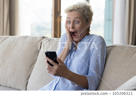 Shocked excited pretty mature woman holding mobile phone Shocked excited pretty mature woman holding mobile phone 105206321
