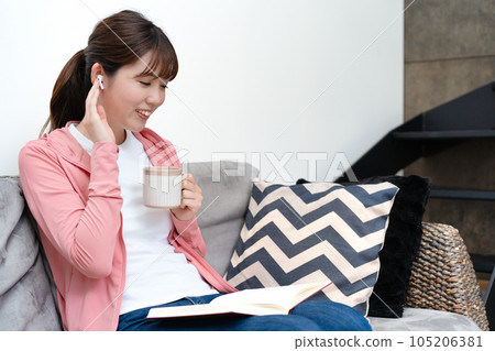 Woman reading a book while listening to music on the sofa 105206381