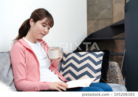 Woman reading a book while listening to music on the sofa 105206383