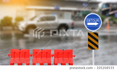 Blue traffic sign with graphic of right detour directional arrow due to flood and red road barriers on blurred flooded street background                               105208535