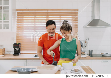 Husband looking at wife who cooking lunch for him. Happy couple in kitchen. 105209205