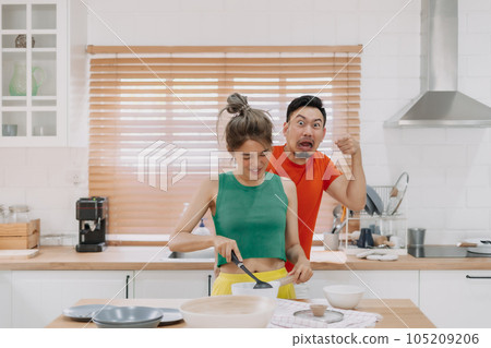 Lover couple. Funny shocked face reaction of husband looking at wife cooking. Lover couple. Funny shocked face reaction of husband looking at wife cooking. 105209206