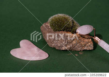 Quartz face roller massager and Gua sha scraper on a stone with growing moss, isolated green background. Spa concept 105209622