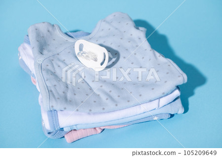 Still life with a baby comforter and clean baby clothes prepared for the birth of child, isolated over blue background 105209649