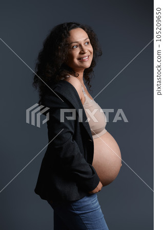 Beautiful authentic gravid woman, holding her pregnant belly, smiling cutely looking aside, isolated on studio backdrop Beautiful authentic gravid woman, holding her pregnant belly, smiling cutely looking aside, isolated on studio backdrop 105209650