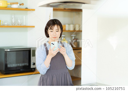 A woman watching a smartphone in the kitchen A woman watching a smartphone in the kitchen 105210751