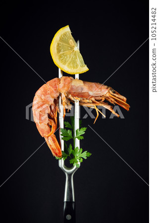 Tiger prawn or king shrimp with parsley and a slice of lemon on a fork. Delicious street or restaurant food idea on black background with space Tiger prawn or king shrimp with parsley and a slice of lemon on a fork. Delicious street or restaurant food idea on black background with space 105214482