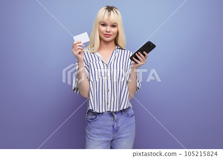 blond 25 year old female person in a striped blouse and jeans pays for the purchase online holding a 105215824