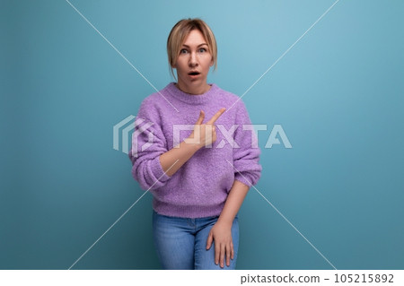 portrait of a shocked surprised blond young woman in a casual look shows her hand to the side on a 105215892