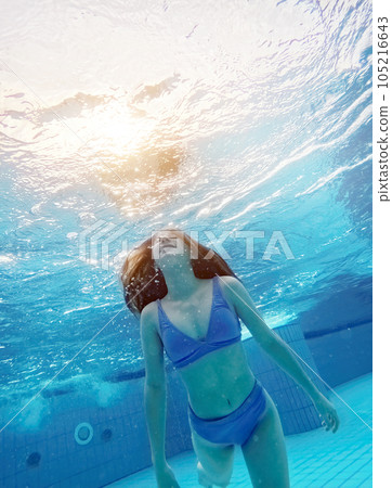 Teen girl swimming under water in blue pool. Pretty female teenager diving and enjoying summer activity Teen girl swimming under water in blue pool. Pretty female teenager diving and enjoying summer activity 105216643