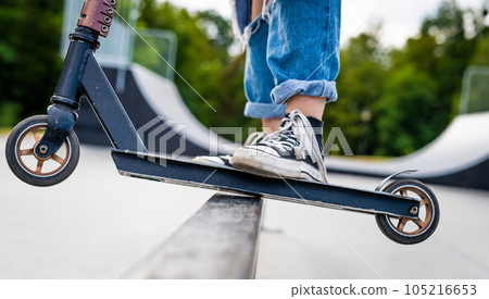 Girl doing tricks on a scooter in a skate park closeup. View on vehicle and person feet. Girl doing tricks on a scooter in a skate park closeup. View on vehicle and person feet. 105216653