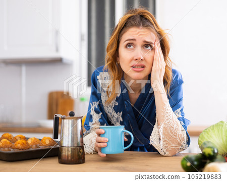 Young woman suffering from migraine, drinking coffee in home kitchen 105219883