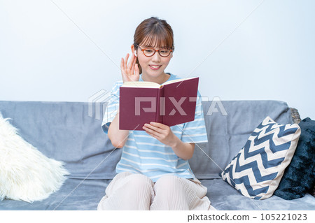 Woman reading a book while listening to music on the sofa 105221023