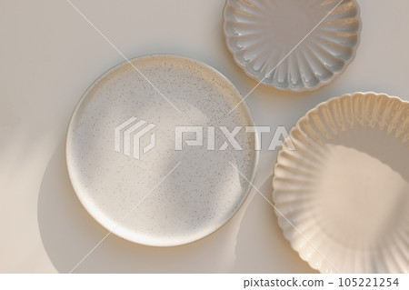 Three different size stoneware plates on beige table background. Flat lay, top view. Natural color disgware. Textured grainy pattern and scallop shaped plates, ceramics. Kitchen, restaurant concept 105221254