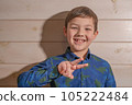 Portrait of a boy 8 years old brunette in a blue shirt. Shows two fingers. 105222484