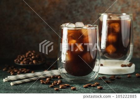 Ice coffee in a tall glass with cream poured over, ice cubes and beans on a dark concrete table. Ice coffee in a tall glass with cream poured over, ice cubes and beans on a dark concrete table. 105222885