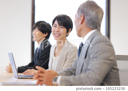 A smiling business woman being spoken to by a man sitting next to her at a seminar_1 105223230
