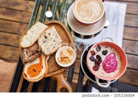 Breakfast with fresh cooked porridge served with Dry Cherry with strawberry sorbet in bowl. Assorted sliced bread on a wooden board. Served with smoked butter. Breakfast with cappuccino coffee. Breakfast with fresh cooked porridge served with Dry Cherry with strawberry sorbet in bowl. Assorted sliced bread on a wooden board. Served with smoked butter. Breakfast with cappuccino coffee. 105226084