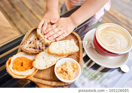 Little girl eats sliced bread. Composition with butter and bread on wooden plate. Breakfast at the bakery cafe. Little girl eats sliced bread. Composition with butter and bread on wooden plate. Breakfast at the bakery cafe. 105226085