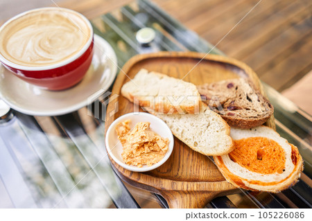 Assorted sliced bread on a wooden board. Served with smoked butter. Breakfast with cappuccino coffee. Composition with butter and bread on wooden plate. 105226086