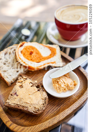 A slice of bread with butter on a chopping board. Assorted sliced bread on a wooden board. Served with smoked butter. Breakfast with cappuccino coffee. A slice of bread with butter on a chopping board. Assorted sliced bread on a wooden board. Served with smoked butter. Breakfast with cappuccino coffee. 105226089