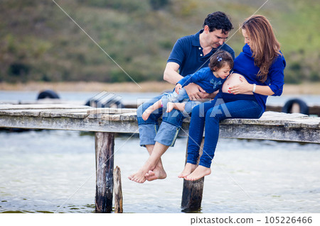 Young couple waiting for their second baby having fun with their baby girl at the beautiful white beach of Lake Tota located in the department of Boyaca at 3,015 meters above sea level in Colombia 105226466