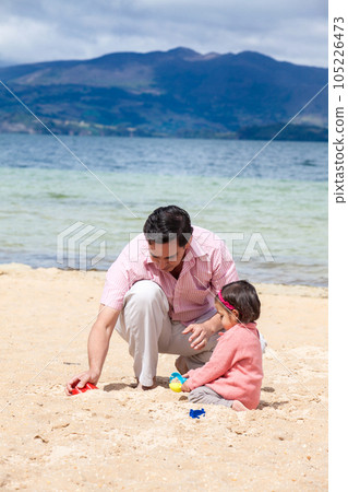 Young father having fun with his baby girl at the beautiful white beach of Lake Tota located in the department of Boyaca at 3,015 meters above sea level in Colombia 105226473