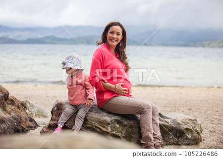 Young pregnant woman having fun with her baby girl at the beautiful white beach of Lake Tota located in the department of Boyaca at 3,015 meters above sea level in Colombia 105226486
