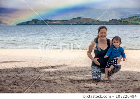 Young pregnant woman having fun with her baby girl at the beautiful white beach of Lake Tota located in the department of Boyaca at 3,015 meters above sea level in Colombia Young pregnant woman having fun with her baby girl at the beautiful white beach of Lake Tota located in the department of Boyaca at 3,015 meters above sea level in Colombia 105226494