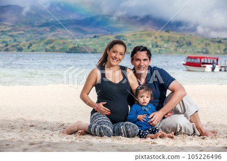 Young couple waiting for their second baby having fun with their baby girl at the beautiful white beach of Lake Tota located in the department of Boyaca at 3,015 meters above sea level in Colombia Young couple waiting for their second baby having fun with their baby girl at the beautiful white beach of Lake Tota located in the department of Boyaca at 3,015 meters above sea level in Colombia 105226496
