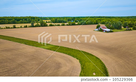 Aerial flat farmland with barren fields and patch of green grass snaking through desert area 105229366