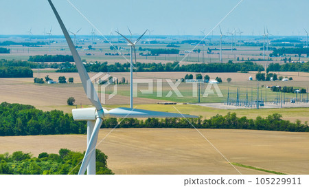 Close up of wind turbine and blades with distant wind farm and substation aerial Close up of wind turbine and blades with distant wind farm and substation aerial 105229911