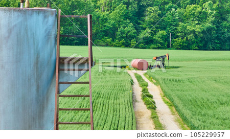 Metal steps and oil pump jack in middle of grass field with maintenance road 105229957