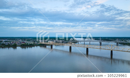 Suspension truss bridges over blue river under deep blue sky leading to distant green shore aerial 105229961